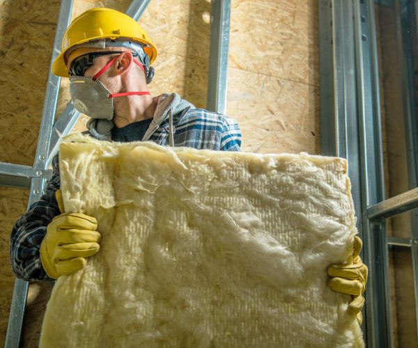 Caucasian Construction Worker Wearing Safety Mask Moving Pieces of Mineral Wool Insulation.